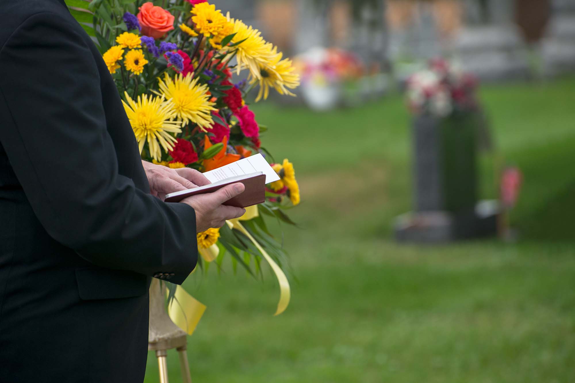 A pastor or minister reads from the Bible during a funeral burial memorial service at a cemetery. Death and grief are a fact of life.