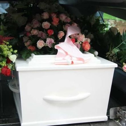 White coffin sitting in the back of a hearse with colourful flowers